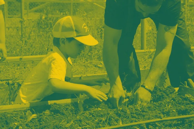 Niño plantando en el huerto con ayuda de un monitor